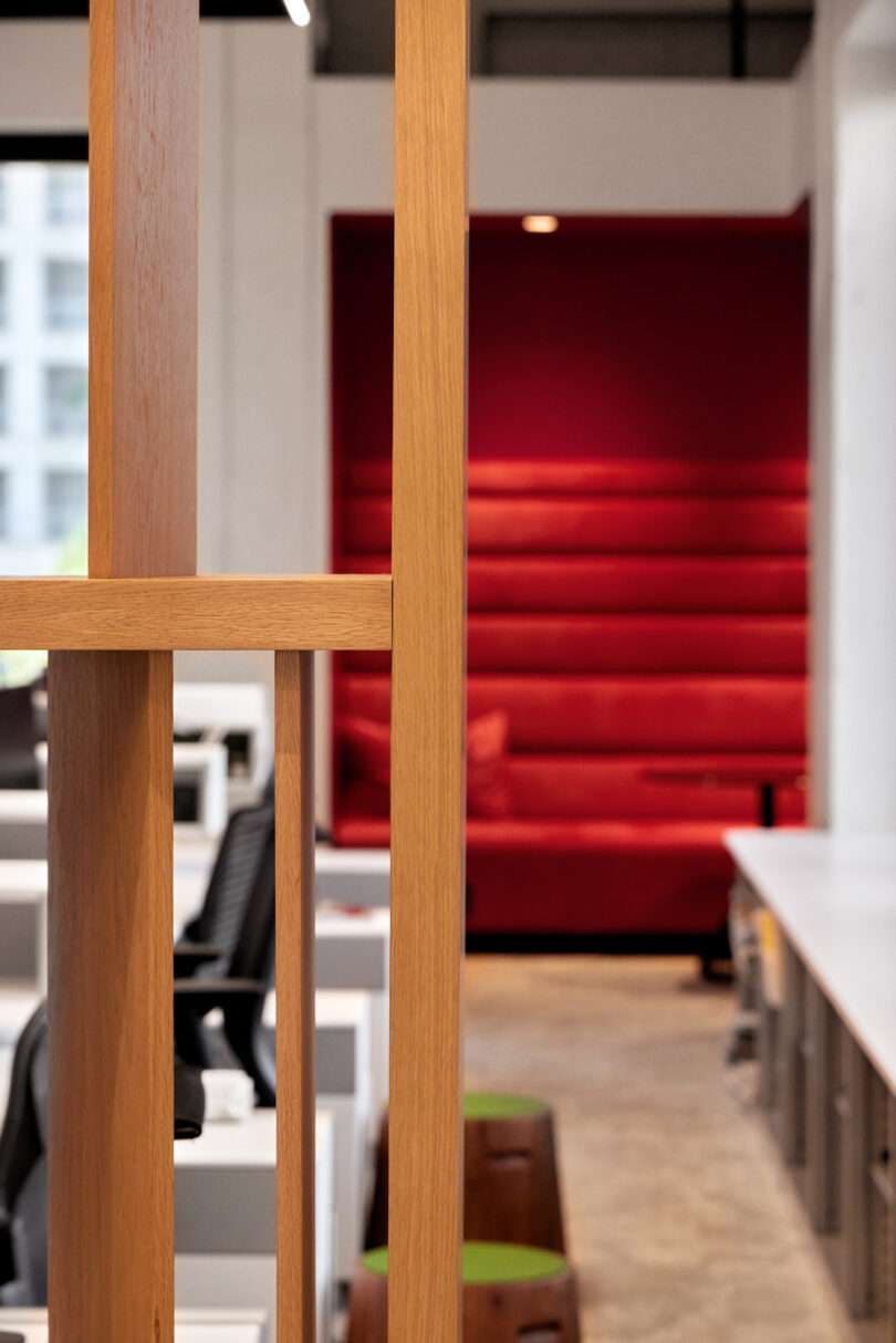 Modern office interior with open white desks, black monitors, and a red seating area in the background, visible through the doorway