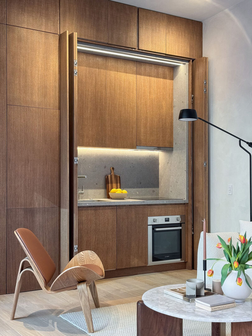 A modern kitchen with wooden cabinets, built-in appliances, and a minimalist Cosmic One ADU living space with a unique chair and decorative elements.