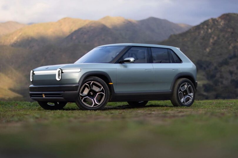 A modern electric suv parked on grass with a backdrop of green hills under a cloudy sky