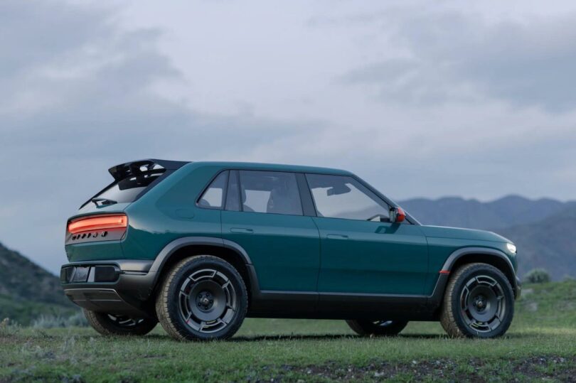 A teal suv parked on a grassy area with hills in the background during twilight