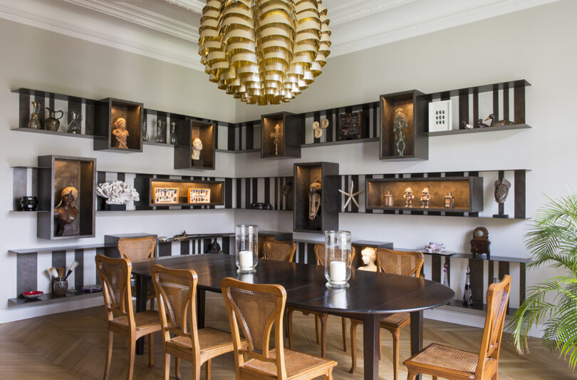 Dining room with a wooden table, matching chairs, and extensive shelving displaying various decorative items and art pieces.