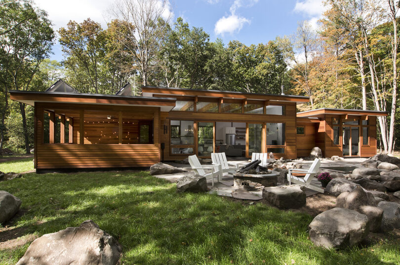 Modern single-story house with large windows, surrounded by a lush green lawn and trees.