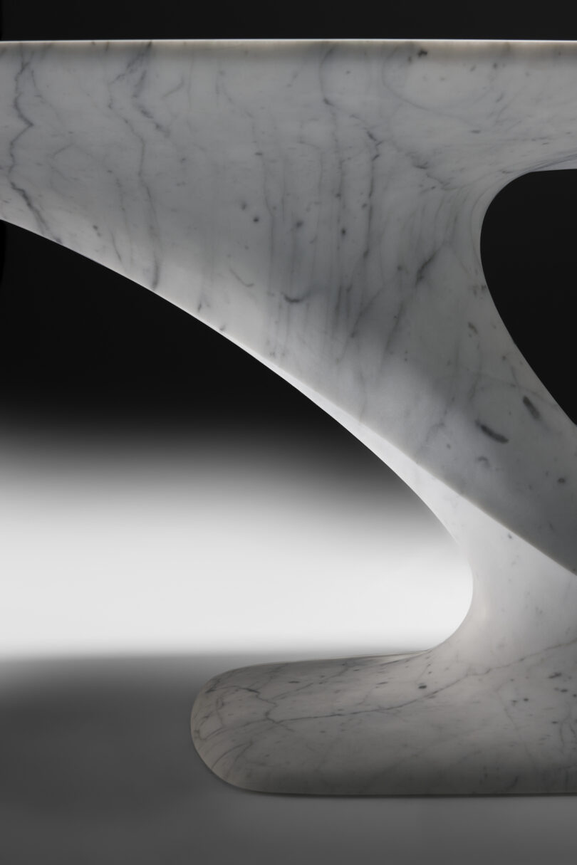 up close details of a modern marble table with a unique v-shaped base and a split, elongated oval top, highlighted against a black background.